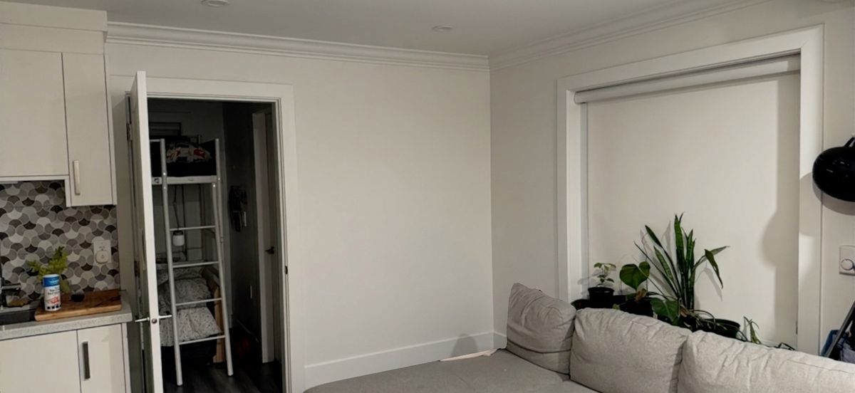 A residential living room with a blank empty wall behind a couch — no shelves, no art, no decoration.