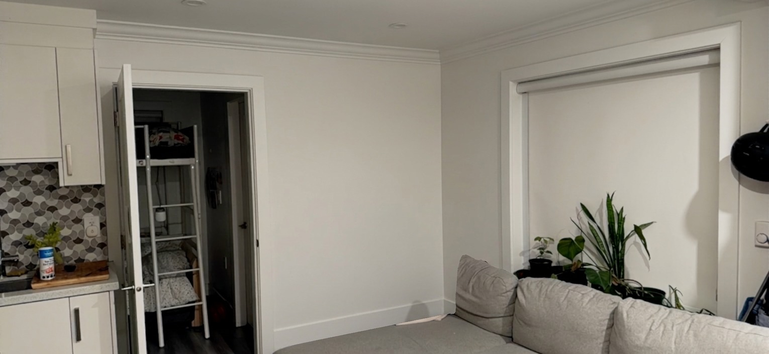 A residential living room with a blank empty wall behind a couch — no shelves, no art, no decoration.