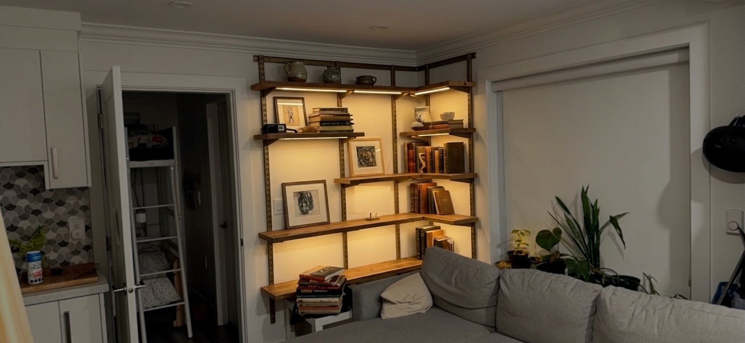 Photorealistic AI-rendered image of warm wooden shelves on rails with integrated lighting, filled with books, art, and pottery, in the same room.