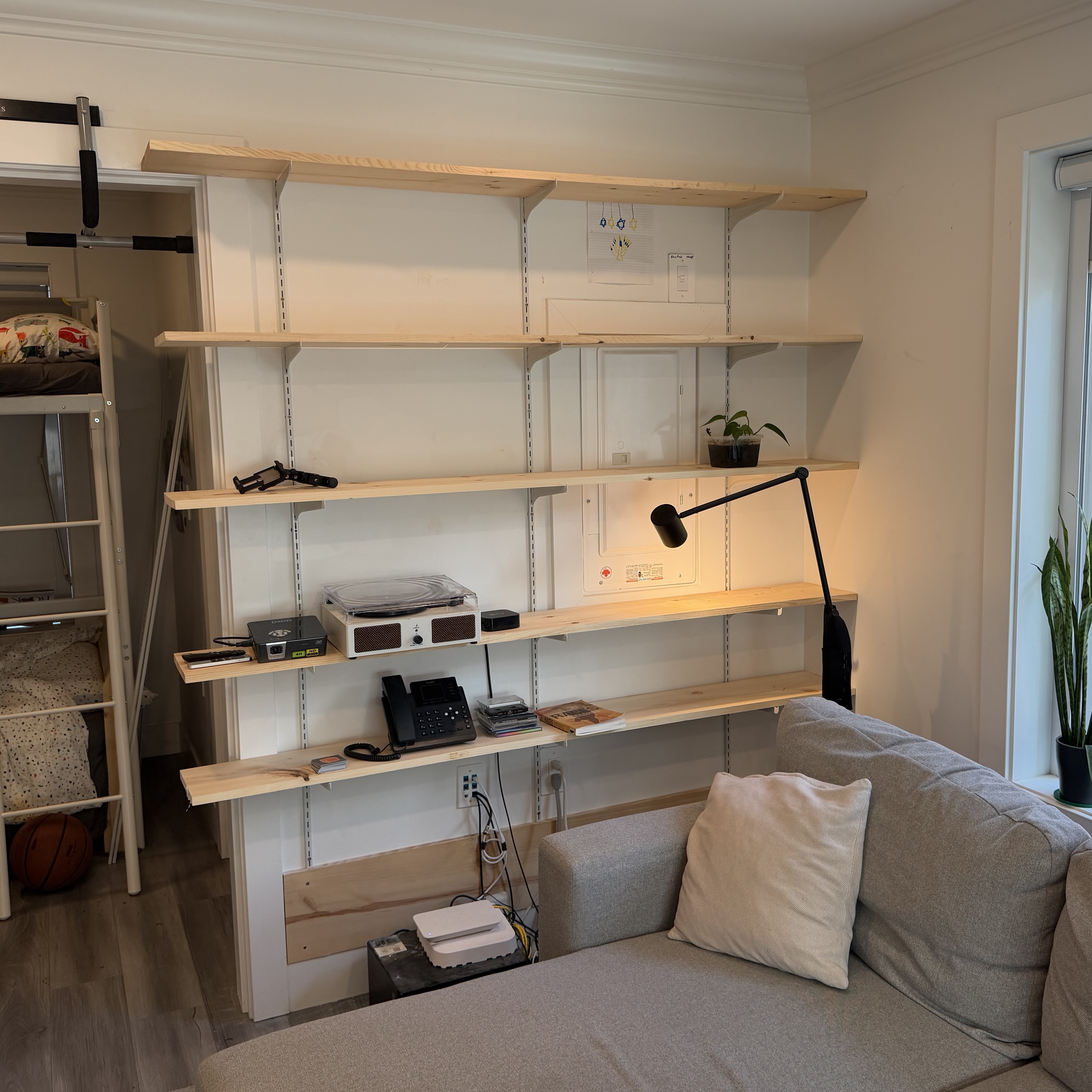 Photograph of the finished wooden shelves on rails with integrated lighting, filled with books, art, and pottery — the actual built result, matching the AI render.
